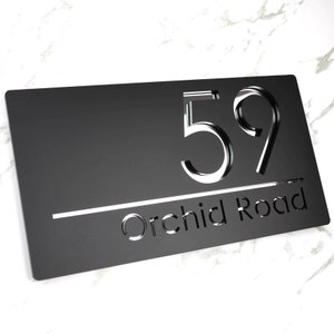 May include: Black house number sign with white cut-out numbers and text. The sign reads "59 Orchid Road".