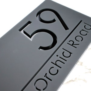 May include: Grey acrylic house number sign with the number 59 and the text "Orchid Road" in a modern font.