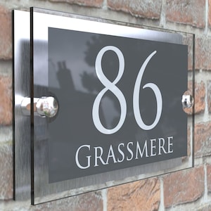 Puede incluir: Un letrero de n&uacute;mero de casa de plata y vidrio con el n&uacute;mero 86 y el nombre Grassmere en letras blancas sobre un fondo gris.