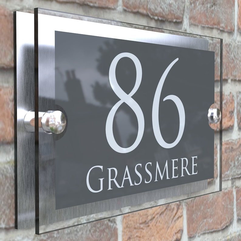 Puede incluir: Un letrero de n&uacute;mero de casa de plata y vidrio con el n&uacute;mero 86 y el nombre Grassmere en letras blancas sobre un fondo gris.