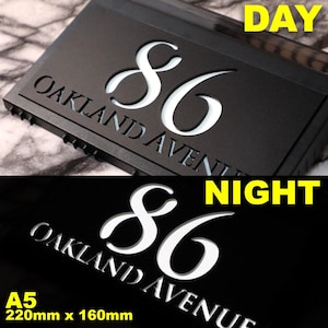 May include: Black house number plaque with white illuminated numbers and text. The plaque reads "86 Oakland Avenue" and is illuminated at night. The plaque is 220mm x 160mm.