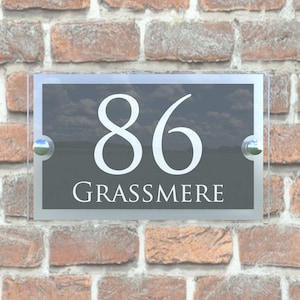 Puede incluir: Un letrero de n&uacute;mero de casa de vidrio con fondo negro y letras blancas. El n&uacute;mero 86 y la palabra "GRASSMERE" se muestran en el letrero.