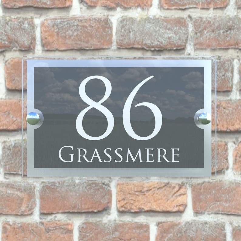 Puede incluir: Un letrero de n&uacute;mero de casa de vidrio con fondo negro y letras blancas. El n&uacute;mero 86 y la palabra "GRASSMERE" se muestran en el letrero.