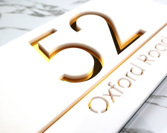 May include: White acrylic house number sign with gold cutout numbers "52" and the text "Oxford Road" underneath.