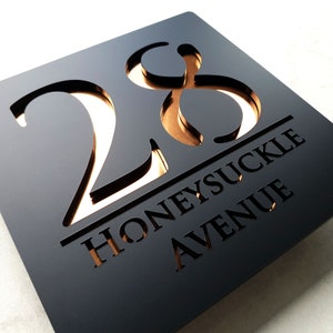 May include: Black house number sign with gold cut-out numbers "28" and the text "Honeysuckle Avenue" in a smaller font.