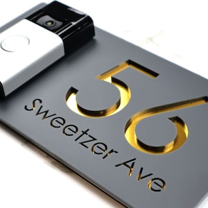 May include: A gray house number sign with gold numbers "56" and the text "Sweetzer Ave" in a modern font.