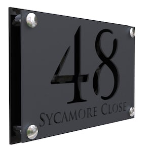 Könnte beinhalten: Ein schwarzes Hausnummernschild aus Metall mit der Nummer 48 ausgeschnitten und den Worten "SYCAMORE CLOSE" darunter graviert. Das Schild hat an jeder Ecke silberne Schrauben.