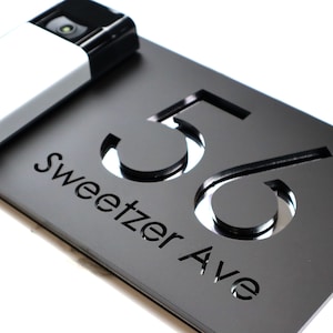 May include: Black house number plaque with the number 56 and the street name "Sweetzer Ave" cut out in a modern font.