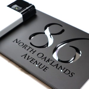 May include: Black house number sign with the number 86 cut out in a decorative font. The sign also has the text "North Oaklands Avenue" engraved in a smaller font.
