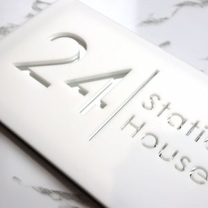 Könnte beinhalten: Weißes Acryl-Hausnummernschild mit der Nummer 24 und dem Text "Station House" in einer verspiegelten Ausführung.