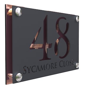 Puede incluir: Un letrero de número de casa de metal negro con el número 48 recortado y las palabras "SYCAMORE CLOSE" debajo. El letrero tiene remaches plateados alrededor de los bordes.