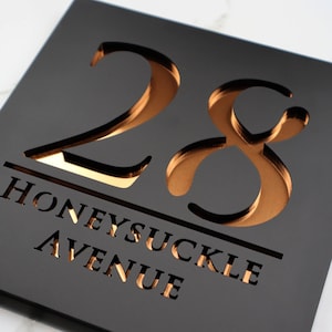 May include: Black house number sign with gold-colored numbers "28" and the text "Honeysuckle Avenue" cut out.