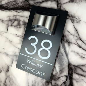 May include: Black house number sign with white text and a silver solar light. The sign reads "38 Willow Crescent".