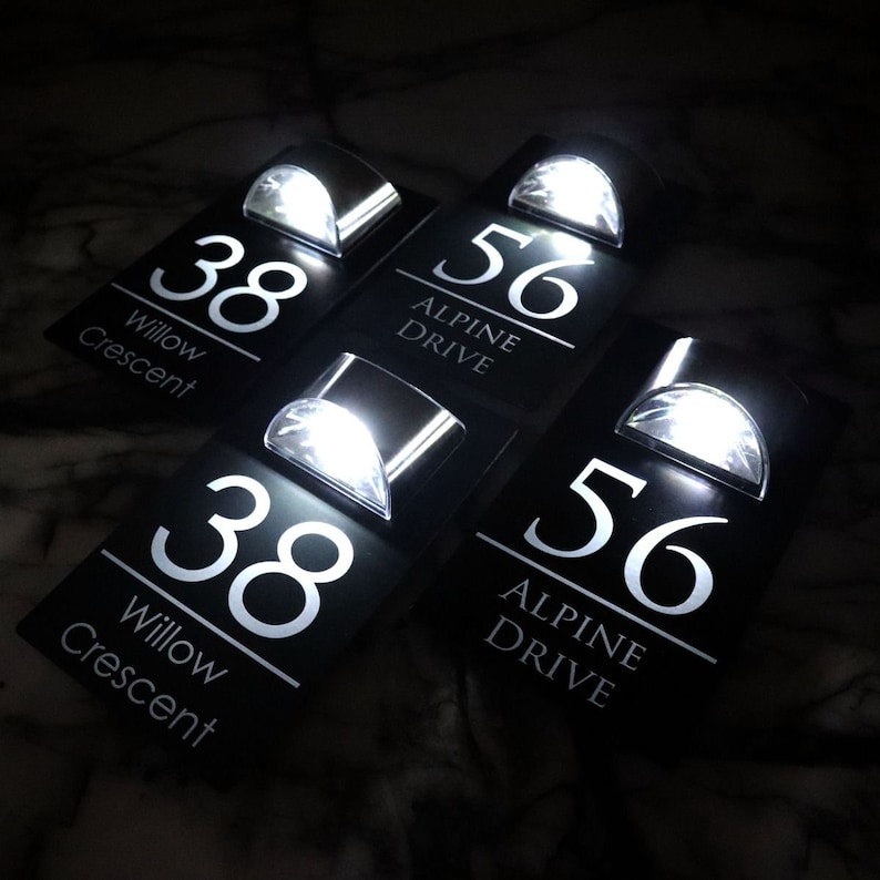 May include: Four black house number plaques with white lettering and built-in LED lights. The plaques read "38 Willow Crescent" and "56 Alpine Drive".