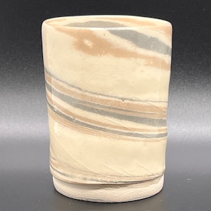 Può includere: Una tazza in ceramica bianca con un motivo a spirale di linee marroni e grigie.