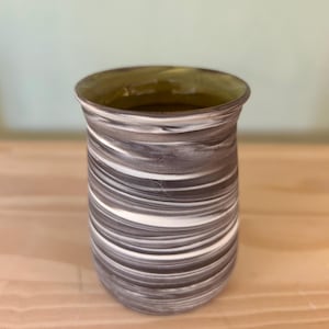 May include: A handcrafted ceramic tumbler with a distinctive swirl design in brown, white, and grey. The inside has a green tint. The cylindrical shape is suitable for drinks.