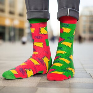 May include: A pair of colourful socks with a geometric pattern of yellow, red and green squares and lines. The socks are worn on a person's feet.