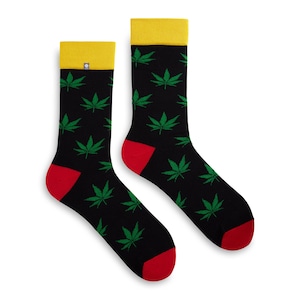 Puede incluir: Un par de calcetines negros con un patrón de hojas de marihuana verdes. Los calcetines tienen un puño amarillo y una punta y un talón rojos.