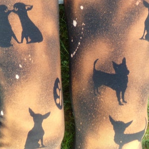 May include: A pair of brown leggings with a black and white splatter paint design. The leggings feature a repeated pattern of black chihuahua silhouettes.