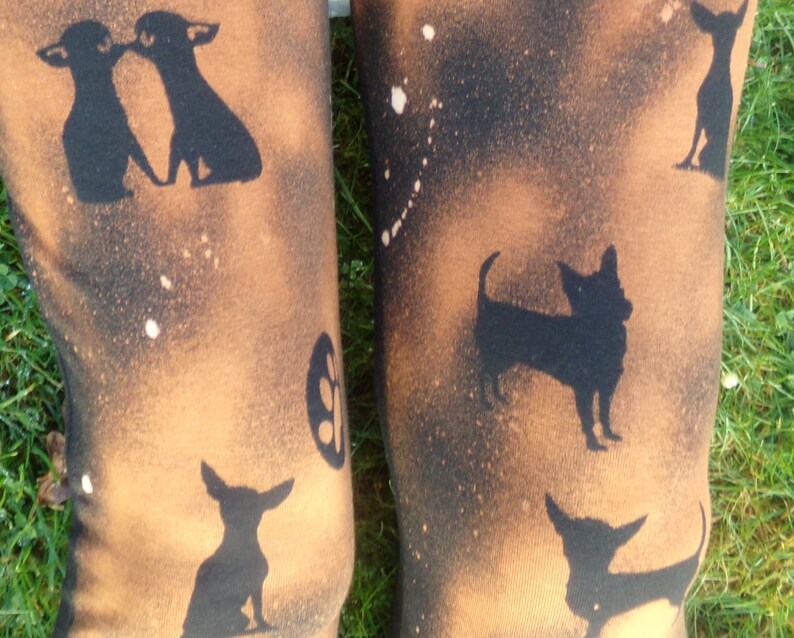 May include: A pair of brown leggings with a black and white splatter paint design. The leggings feature a repeated pattern of black chihuahua silhouettes.