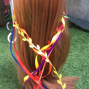 Könnte beinhalten: Ein rotes, gelbes, blaues und violettes Band-Haarband mit weißen Papierblättern. Das Haarband wird auf einer rotbraunen Perücke getragen.
