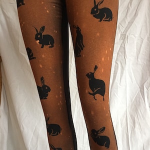 Peut inclure: Collants marron avec un motif de silhouettes de lapins noirs et des mouchetures blanches. Gros plan sur le tissu. Thème : mode fantaisiste avec des animaux. Les détails du motif et la texture du tissu sont bien visibles.