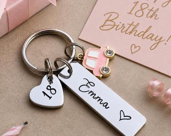 May include: A silver-toned metal keychain featuring a rectangular tag engraved with the name Emma and a heart, a heart-shaped charm engraved with the number 18, and a small pink car charm with two clear rhinestones attached to a circular ring.