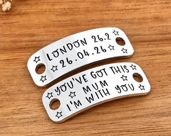 May include: Two silver-colored metal shoe tags with rounded corners and two circular holes on each side. The top tag is engraved with LONDON 26.2 and 26.04.26. The bottom tag is engraved with YOU'VE GOT THIS MUM I'M WITH YOU. Both feature star motifs.