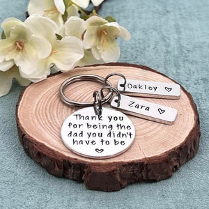 May include: Silver keychain with a round charm that reads "Thank you for being the dad you didn't have to be" and two smaller charms that read "Oakley" and "Zara".