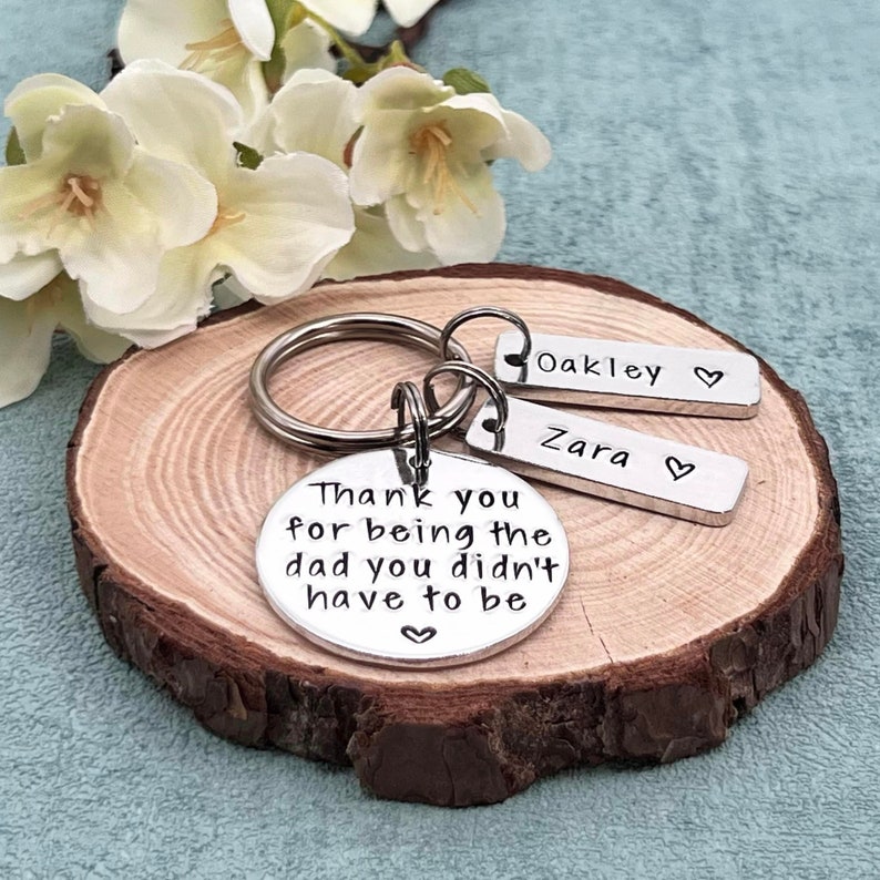 May include: Silver keychain with a round charm that reads "Thank you for being the dad you didn't have to be" and two smaller charms that read "Oakley" and "Zara".