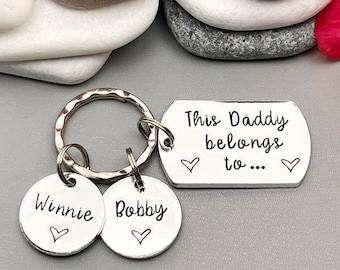 May include: Silver keychain with a tag that reads "This Daddy belongs to..." with two small hearts on either side.  The keychain has two round tags with the names "Winnie" and "Bobby" on them, each with a small heart.