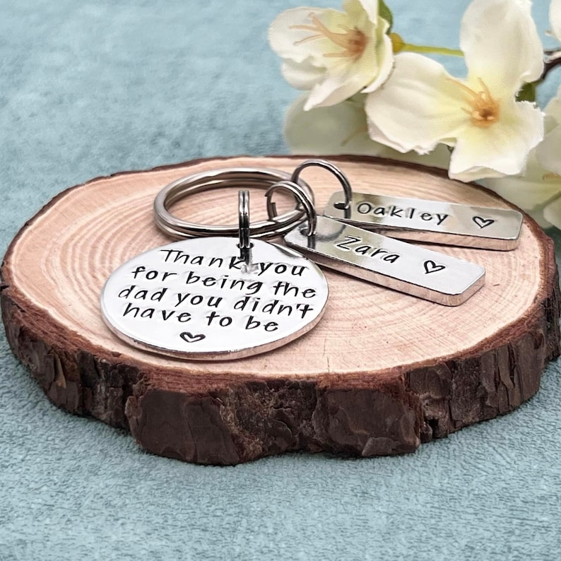 May include: Silver keychain with a round charm that reads "Thank you for being the dad you didn't have to be". There are two smaller charms that read "Zara" and "Oakley".