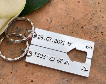 Könnte beinhalten: Silberner Schlüsselanhänger mit zwei ineinandergreifenden Teilen, jedes mit einem Datum und einem Pfeil. Das obere Teil zeigt "29.07.2021" mit einem Herzsymbol. Das untere Teil zeigt "29.07.2021" mit einem Pfeil, der nach rechts zeigt.