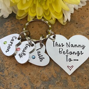 May include: Silver heart-shaped keychain with the text "This Nanny Belongs To..." and three smaller heart-shaped charms with the names "Carson", "Emily", and "Faith".
