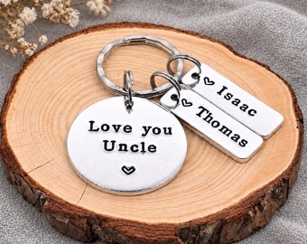 May include: A silver-toned metal keychain featuring a large circular charm engraved with the text "Love you Uncle" and a small heart symbol, accompanied by two rectangular charms engraved with the names "Isaac" and "Thomas" each with a heart.