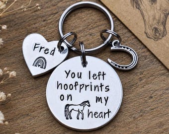 May include: A silver-toned metal keychain featuring a circular disc engraved with the text 'You left hoofprints on my heart' and a horse graphic, a heart-shaped charm stamped with 'Fred' and a rainbow, and a small horseshoe charm on a split ring.