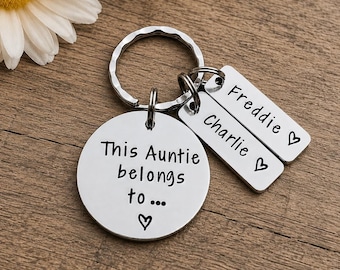May include: A silver-toned metal keychain featuring a large circular disc engraved with the text 'This Auntie belongs to...' and a small heart. Two smaller rectangular silver-toned tags are attached, each engraved with a name, 'Charlie' and 'Freddie', and a heart.