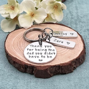 May include: Silver keychain with a round charm that reads "Thank you for being the dad you didn't have to be" and two smaller charms that read "Oakley" and "Zara".