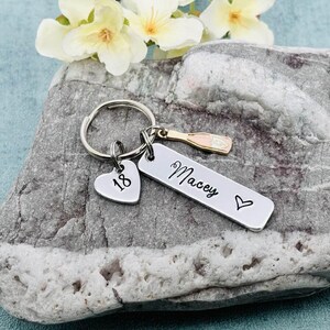 May include: Silver keyring with a heart charm that says "18", a charm of a champagne bottle, and a bar charm that says "Macey" with a heart.