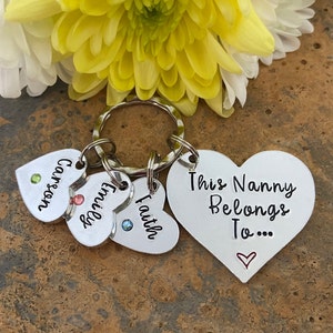 May include: Silver heart-shaped keychain with the text "This Nanny Belongs To..." and three smaller heart-shaped charms with the names "Carson", "Emily", and "Faith".
