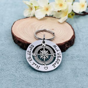 May include: Silver compass keychain with coordinates 27°53.7'N 88°57.1'W engraved on the front. The compass features a black and silver design with a heart symbol.