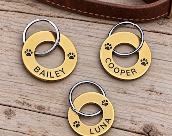May include: Three circular gold-toned metal pet ID tags, each featuring a silver split ring. The tags are engraved with the names BAILEY, COOPER, and LUNA, accompanied by small black paw print icons on the surface of each round metal disc.