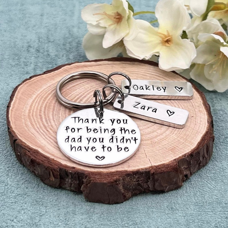May include: Silver keychain with a round charm that reads "Thank you for being the dad you didn't have to be" and two smaller charms that read "Oakley" and "Zara".