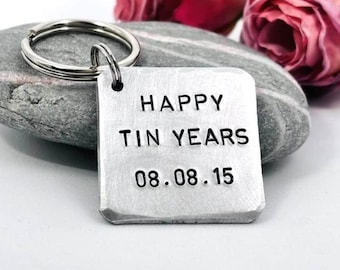 May include: A square, brushed metal keyring featuring the stamped black text HAPPY TIN YEARS and the date 08.08.15. The metal tag is attached to a circular silver-toned split ring, showcasing a textured surface and rounded corners.