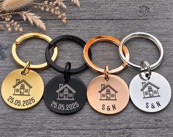 May include: Four circular metal keychains in gold, black, rose gold, and silver tones. Each keychain features a laser-engraved line drawing of a house. Two keychains display the date 25.05.2025, while the other two are engraved with the letters S & N.