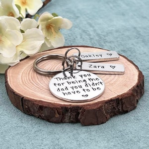 May include: Silver keychain with a round charm that reads "Thank you for being the dad you didn't have to be" and two smaller charms that read "Oakley" and "Zara".
