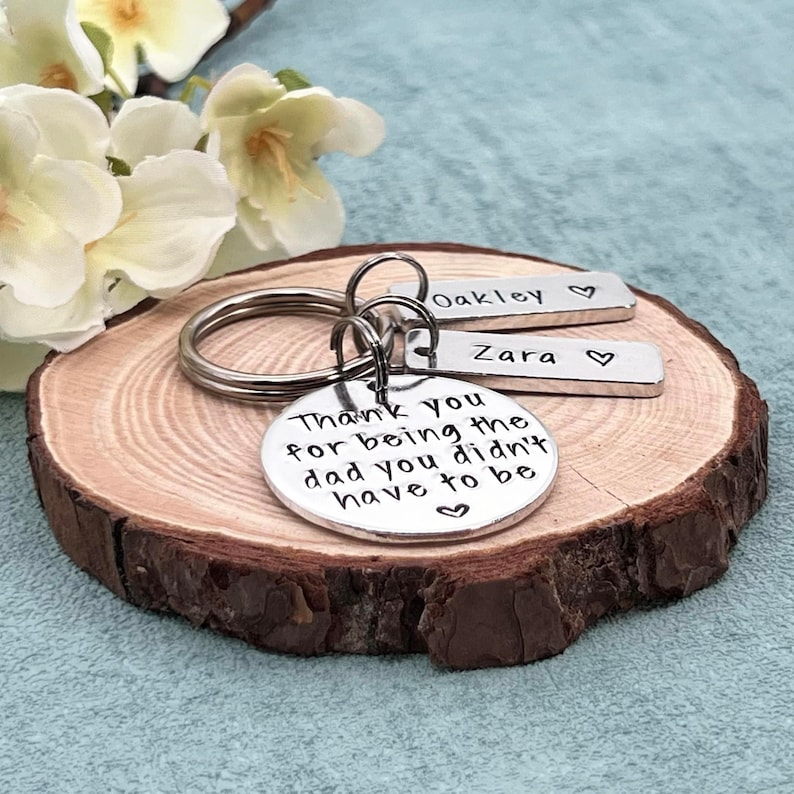 May include: Silver keychain with a round charm that reads "Thank you for being the dad you didn't have to be" and two smaller charms that read "Oakley" and "Zara".