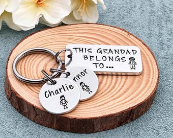 May include: A silver-toned metal keychain featuring a rectangular tag engraved with the text THIS GRANDAS BELONGS TO and a stick figure, along with two circular tags engraved with the names Charlie and Connor and corresponding stick figures.