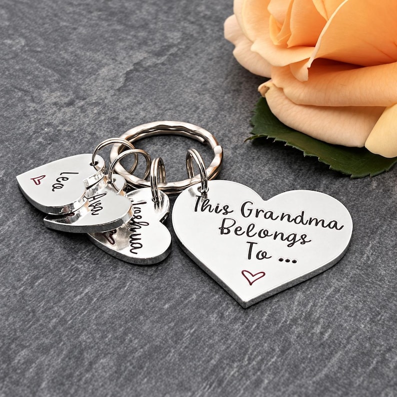Pode incluir: Um porta-chaves de metal prateado com um pendente grande em forma de cora&ccedil;&atilde;o gravado com o texto This Grandma Belongs To... e tr&ecirc;s pendentes mais pequenos em forma de cora&ccedil;&atilde;o com os nomes Lea, Ava e Joshua, cada um com um pequeno cora&ccedil;&atilde;o.