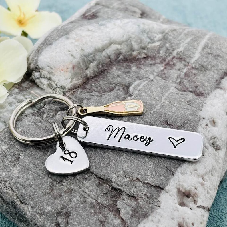 May include: Silver keyring with a heart charm, a champagne bottle charm, and a tag that says "Macey" with the number "18" on the heart charm.